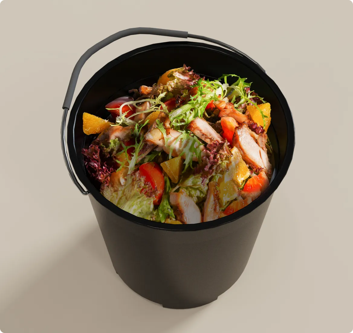 Un cubo de cocina negro lleno de residuos alimentarios variados como lechuga, carne y verduras representa los residuos domésticos típicos del día a día.